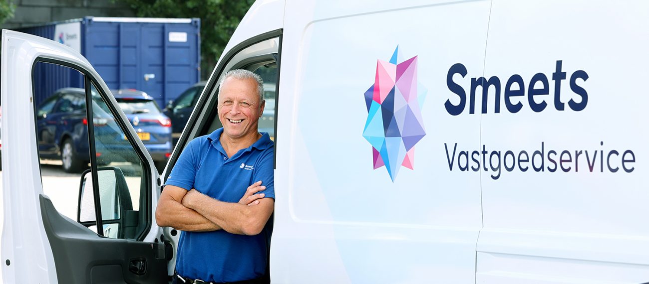 Medewerker poseert lachend bij bedrijfsbus van vastgoedservicebedrijf