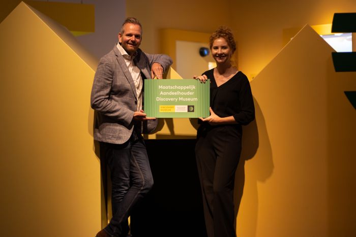 Twee mensen poseren met een bord waarop staat "Maatschappelijk Aandeelhouder Discovery Mseum"