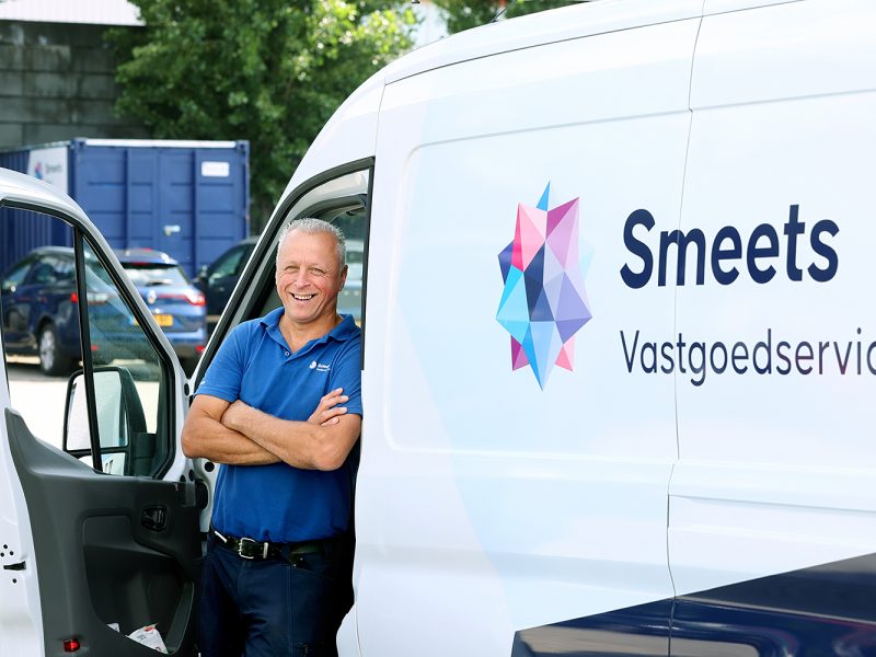 Medewerker poseert lachend bij bedrijfsbus van vastgoedservicebedrijf
