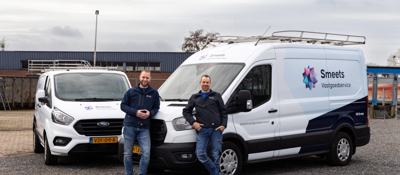 Twee mannen staan voor witte bedrijfswagens op een industrieterrein.