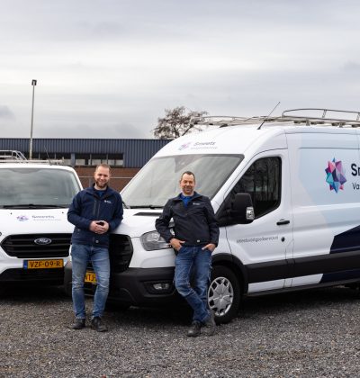 Twee mannen staan voor witte bedrijfswagens op een industrieterrein.