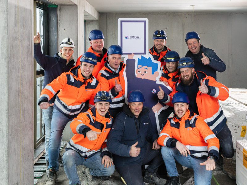 Een enthousiaste groep collega's poseert met mascotte Bobby in het midden