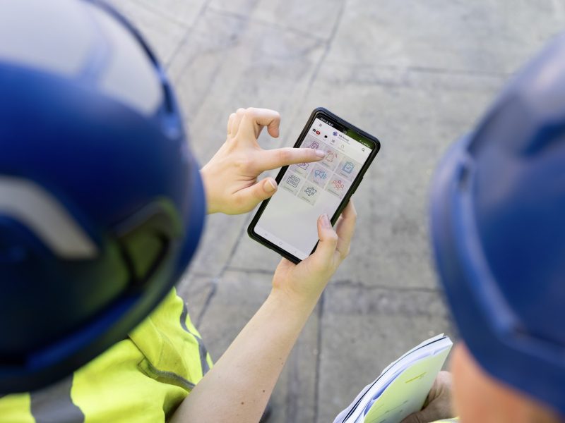 Twee mensen zijn van bovenaf te zien waarbij een van de twee een smart phone vasthoud, waarop de VB Portal App is te zien